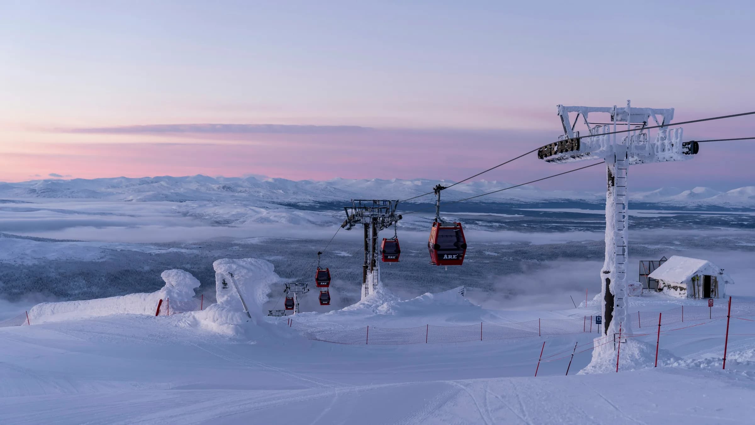 Soluppgång över snöklädda fjäll sedd från Åreskutan, med kabinbanans röda gondoler i förgrunden.