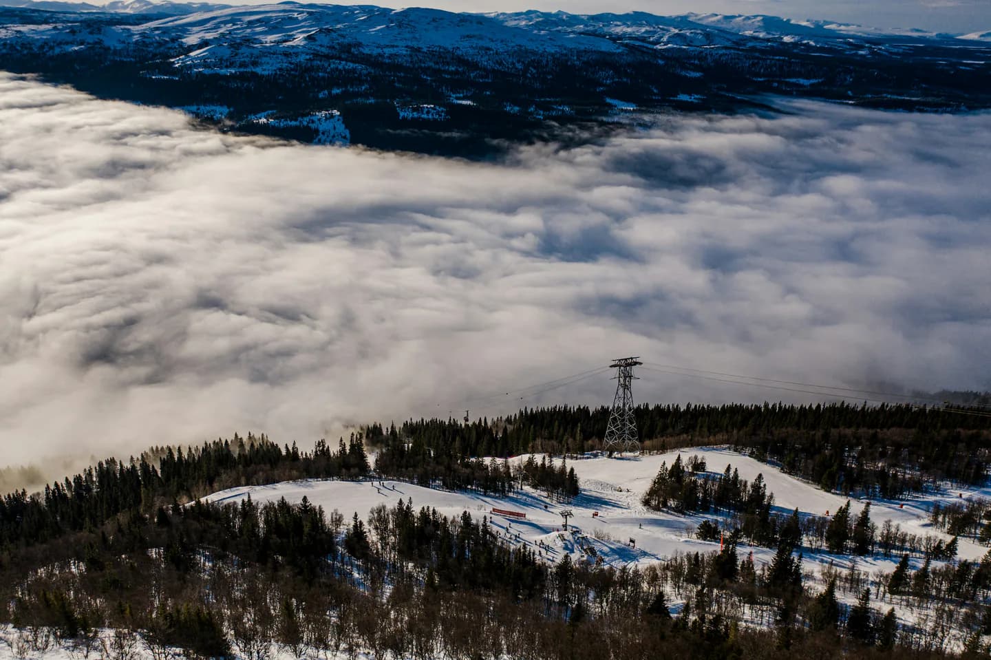 Moln som fyller dalgången nedanför snöklädda fjällsluttningar.