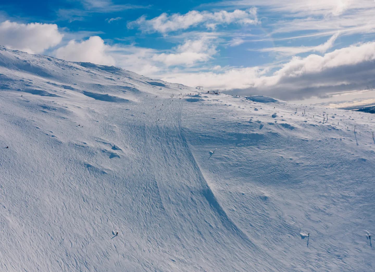 Skidspår i orörd snö nedför en fjällsluttning under blå himmel.