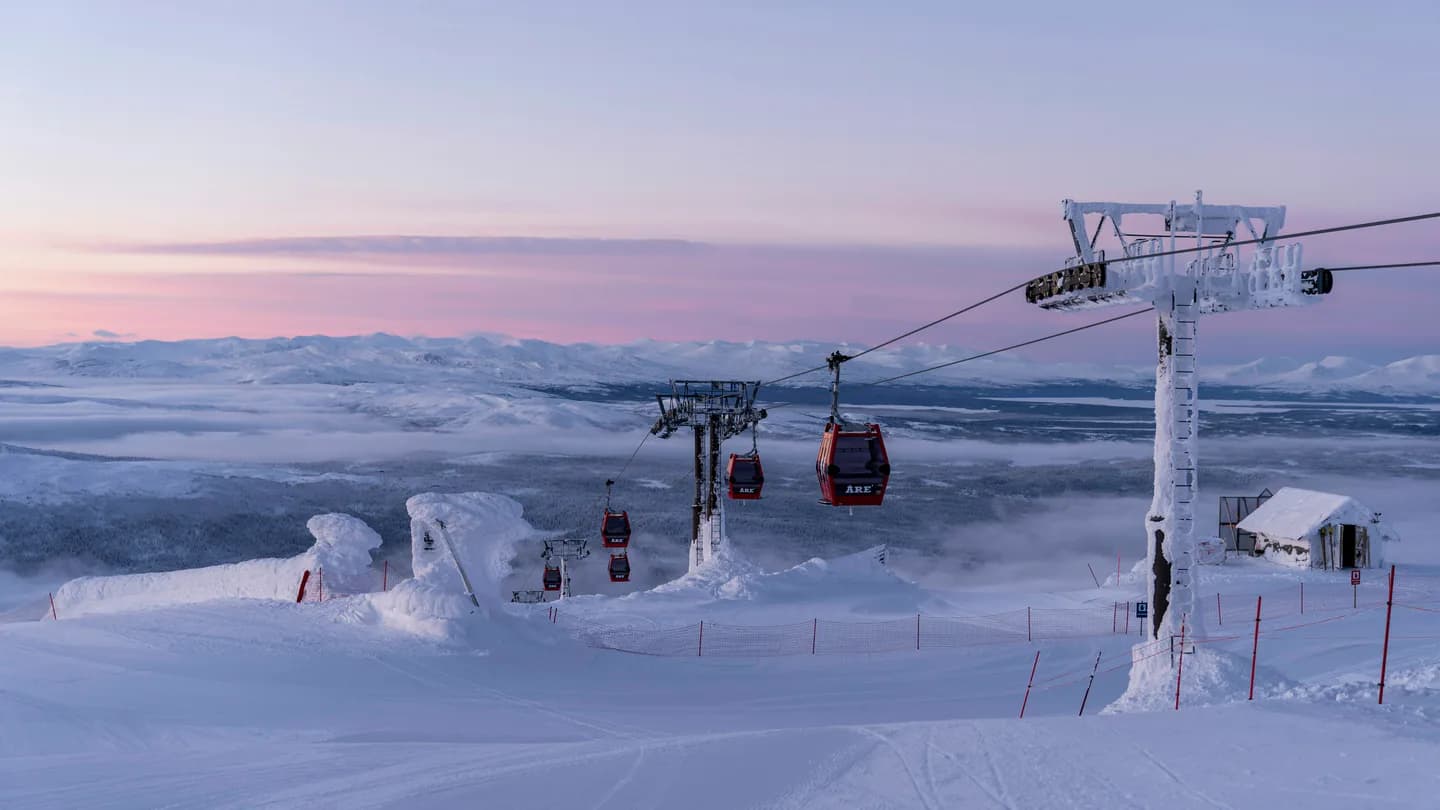 Soluppgång över snöklädda fjäll sedd från Åreskutan, med kabinbanans röda gondoler i förgrunden.
