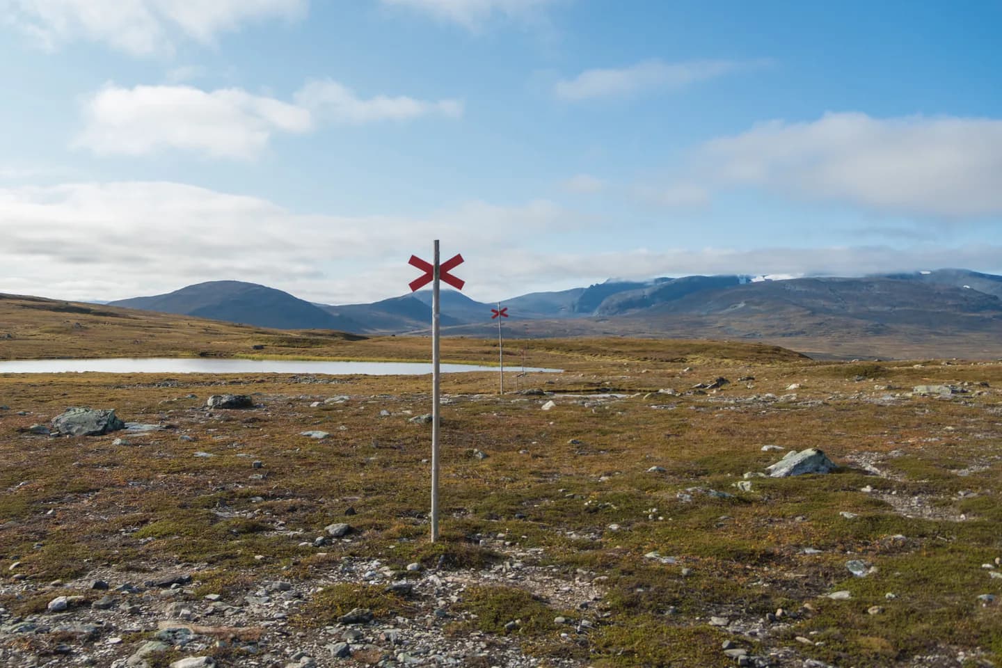 Rött ledkryss på en stolpe i en fjälldal med vida vidder.